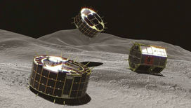 Художественное изображение роверов  MINERVA II-1 (слева и в центре) и готовящегося к посадке MINERVA II-2 (справа) на поверхности астероида.